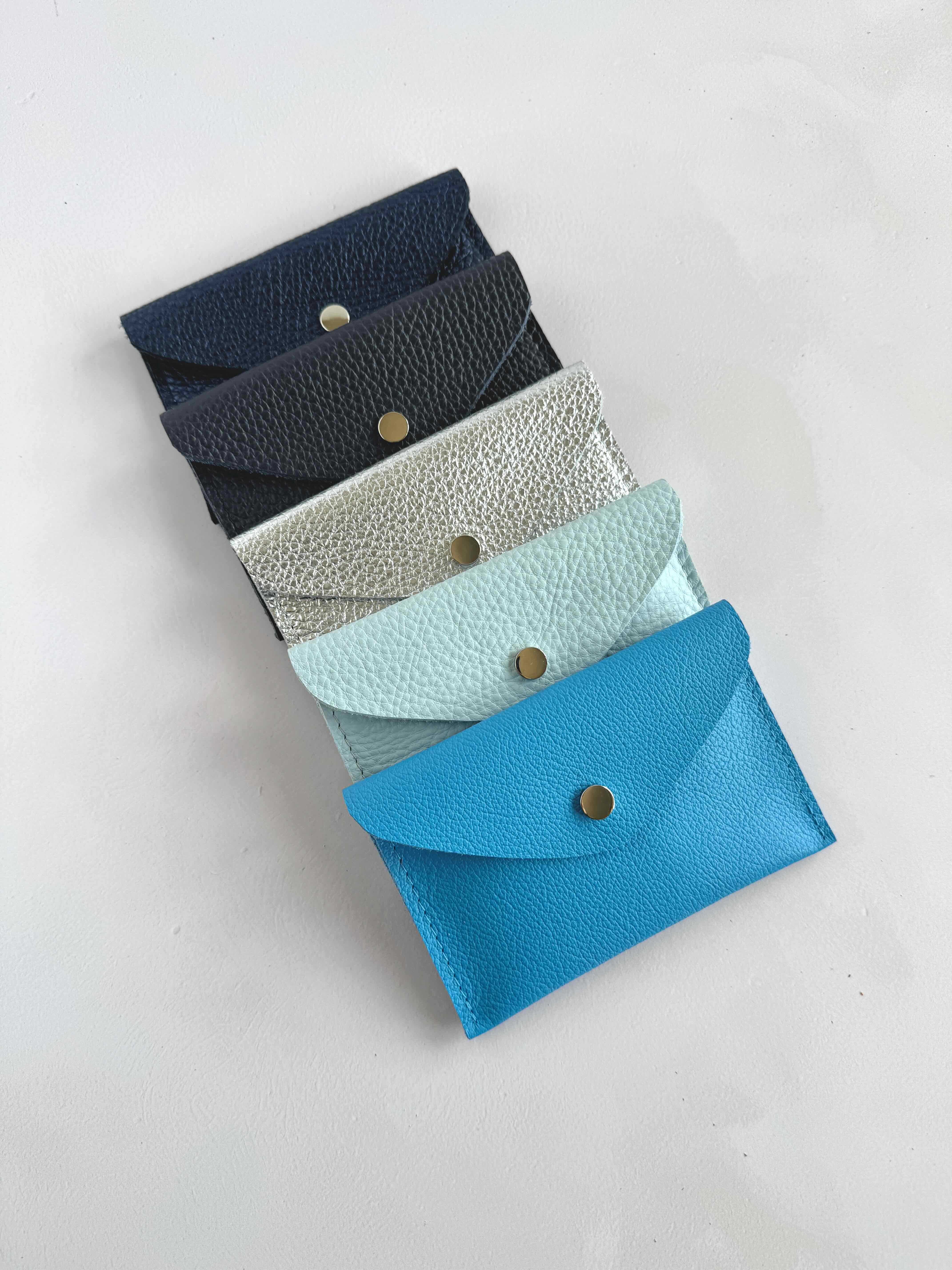 A collection of leather envelopes in various shades of blue, navy, and light blue, arranged in a stack with the front envelope opened to show the interior.