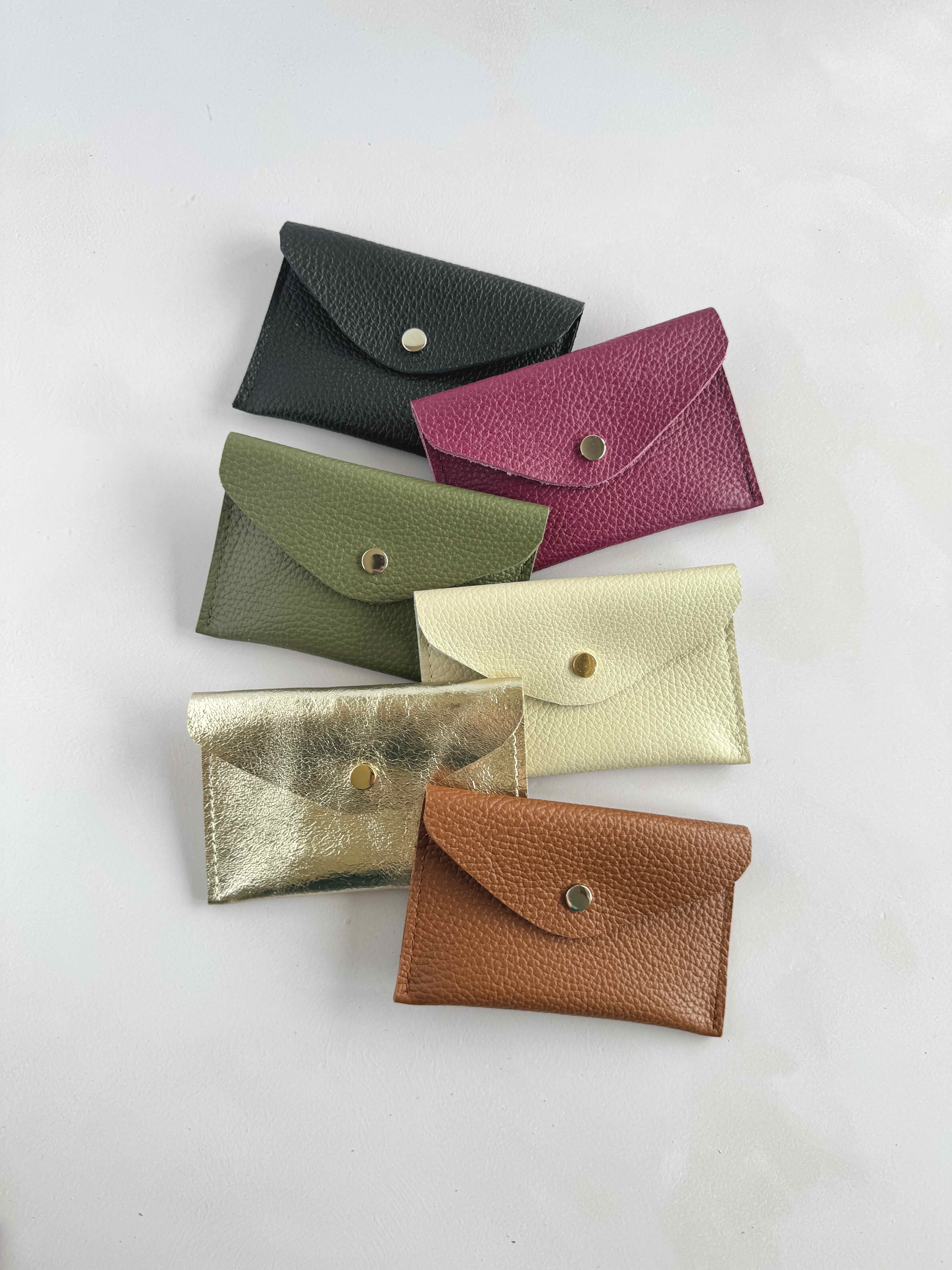 A collection of envelope leather purses in black, tan, khaki, and gold colors displayed against a white background.