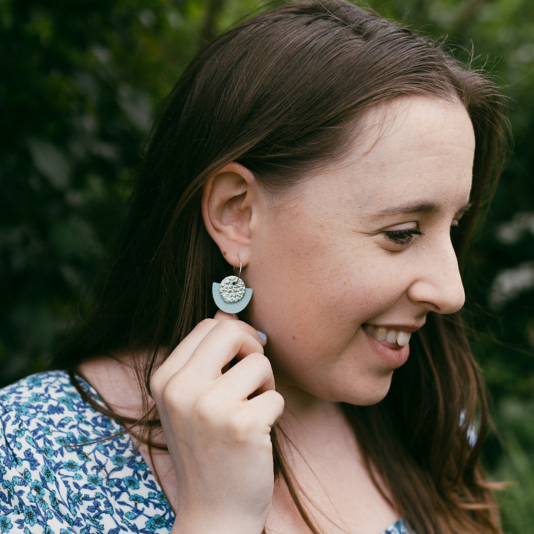 Woman wearing a blue floral dress and earrings, standing against a green leafy background