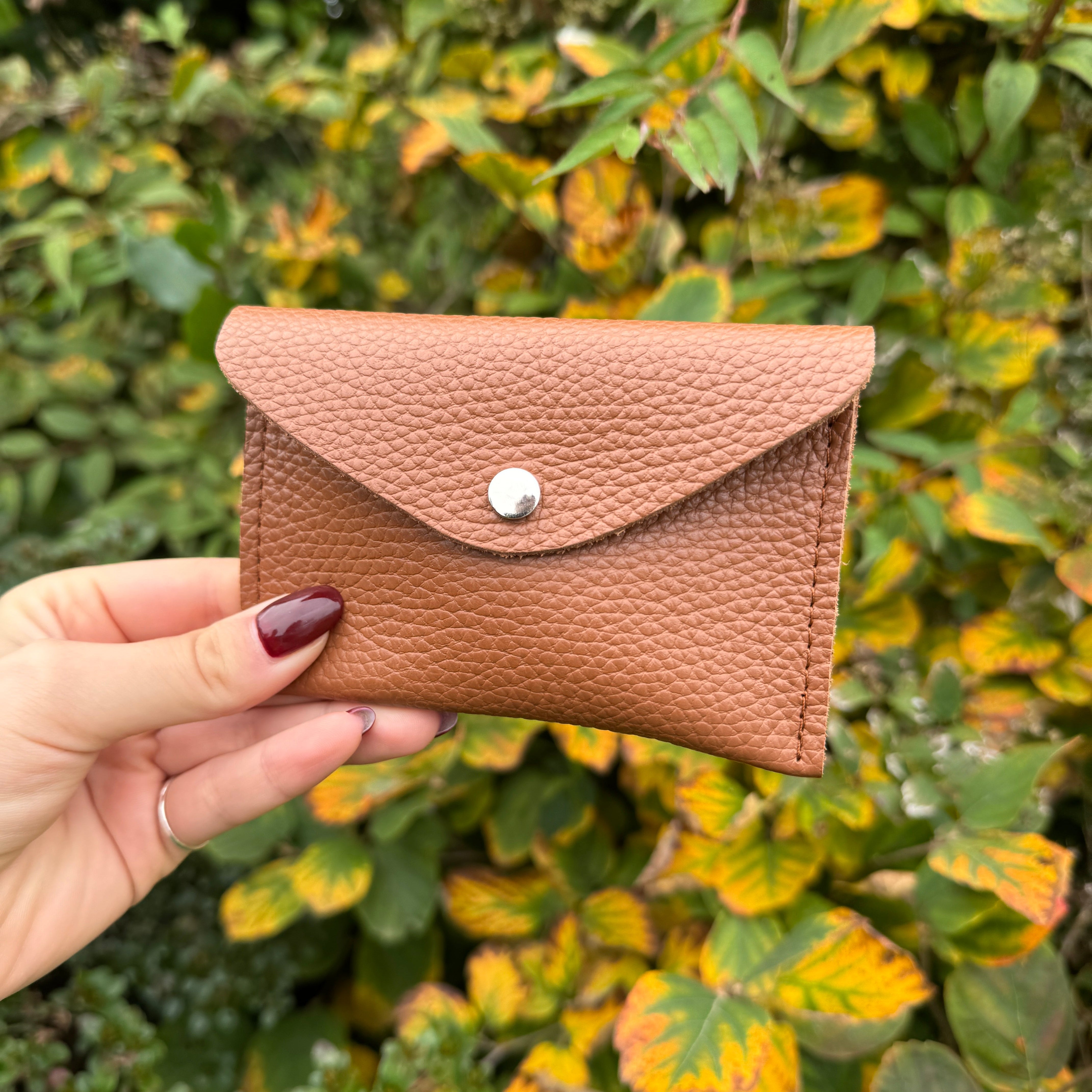 Brown leather cardholder held in front of a green leafy background