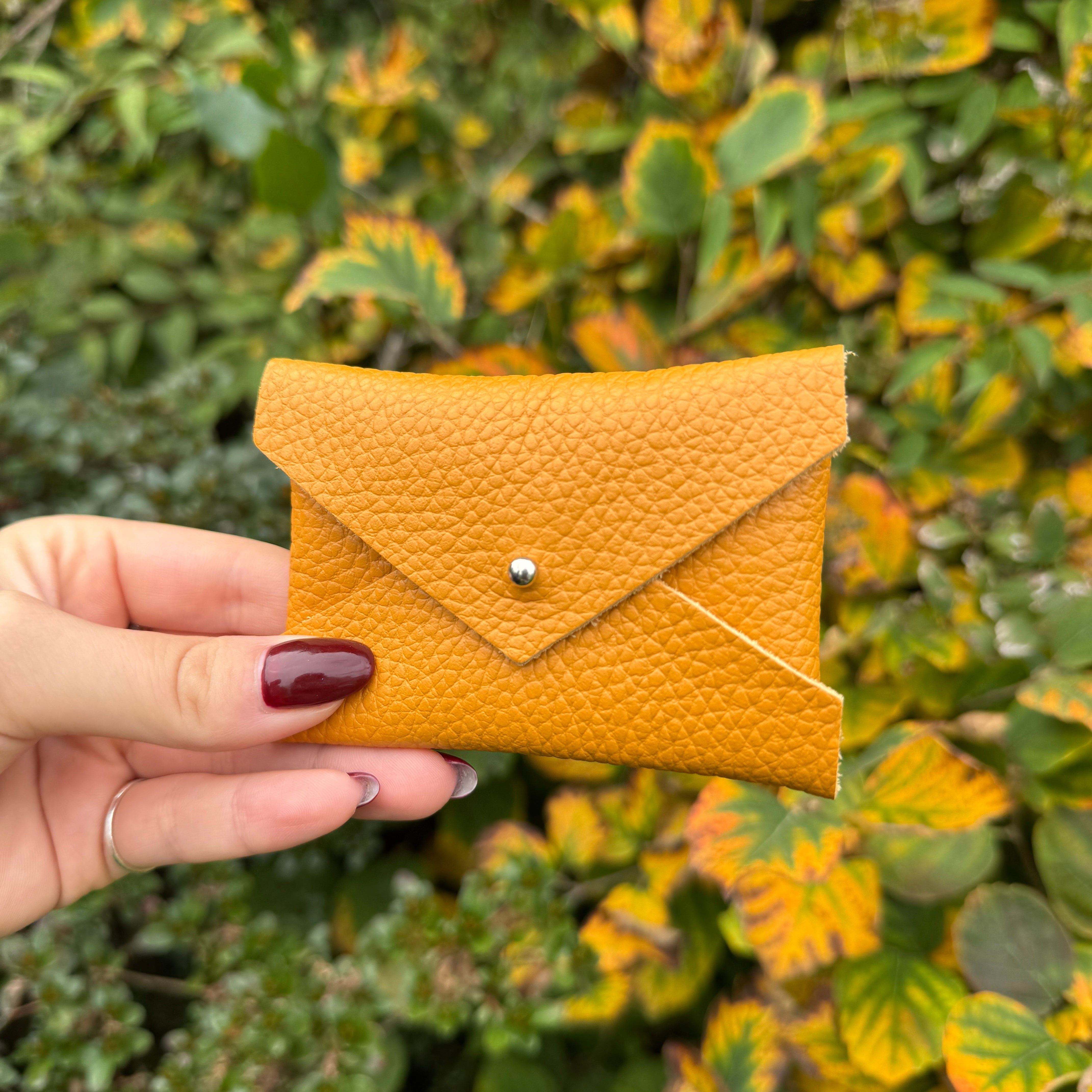 Hand holding a pumpkin spice leather pouch against a green leafy background