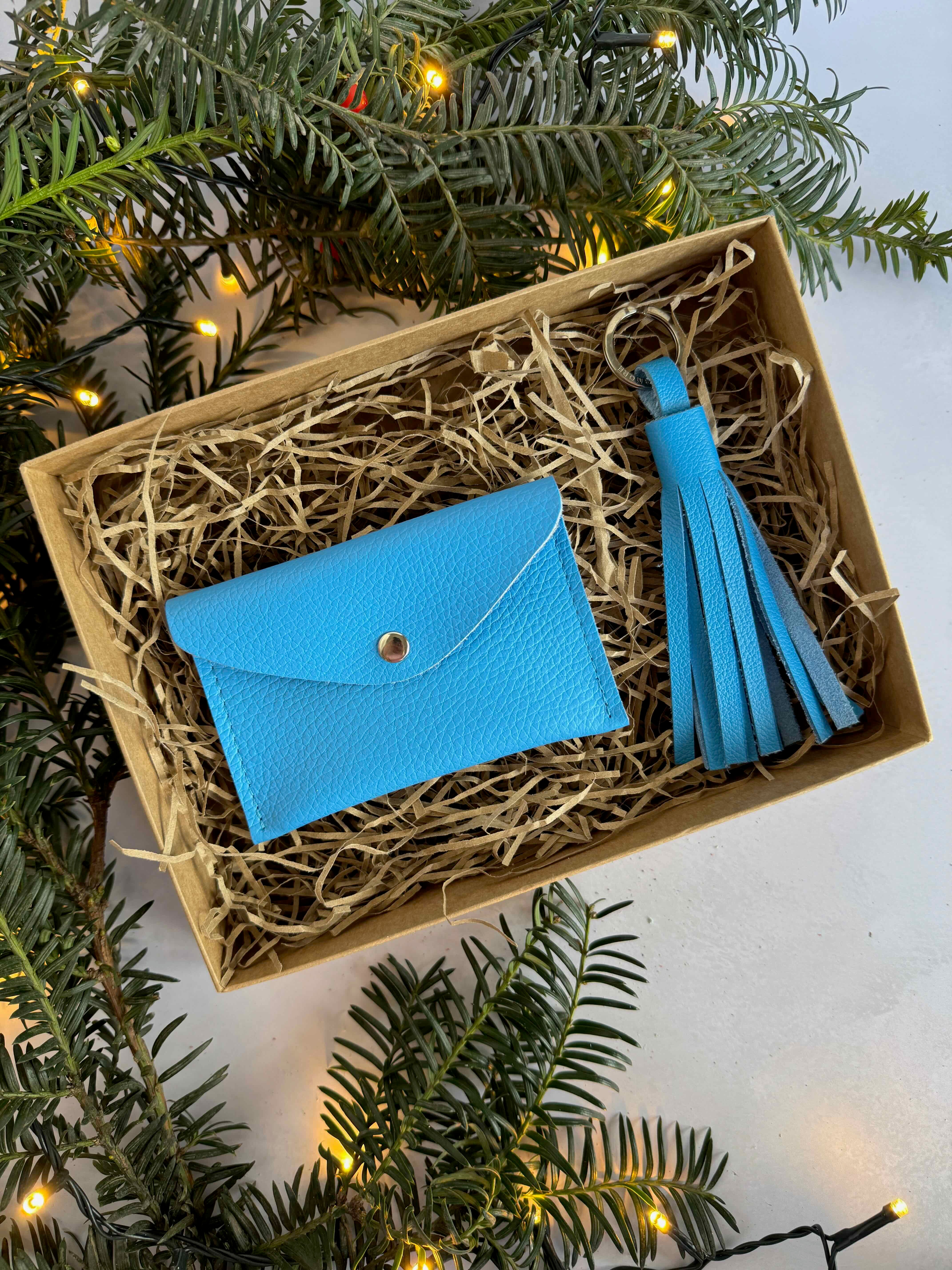Blue cardholder with tassel in a decorative box surrounded by Christmas tree branches.