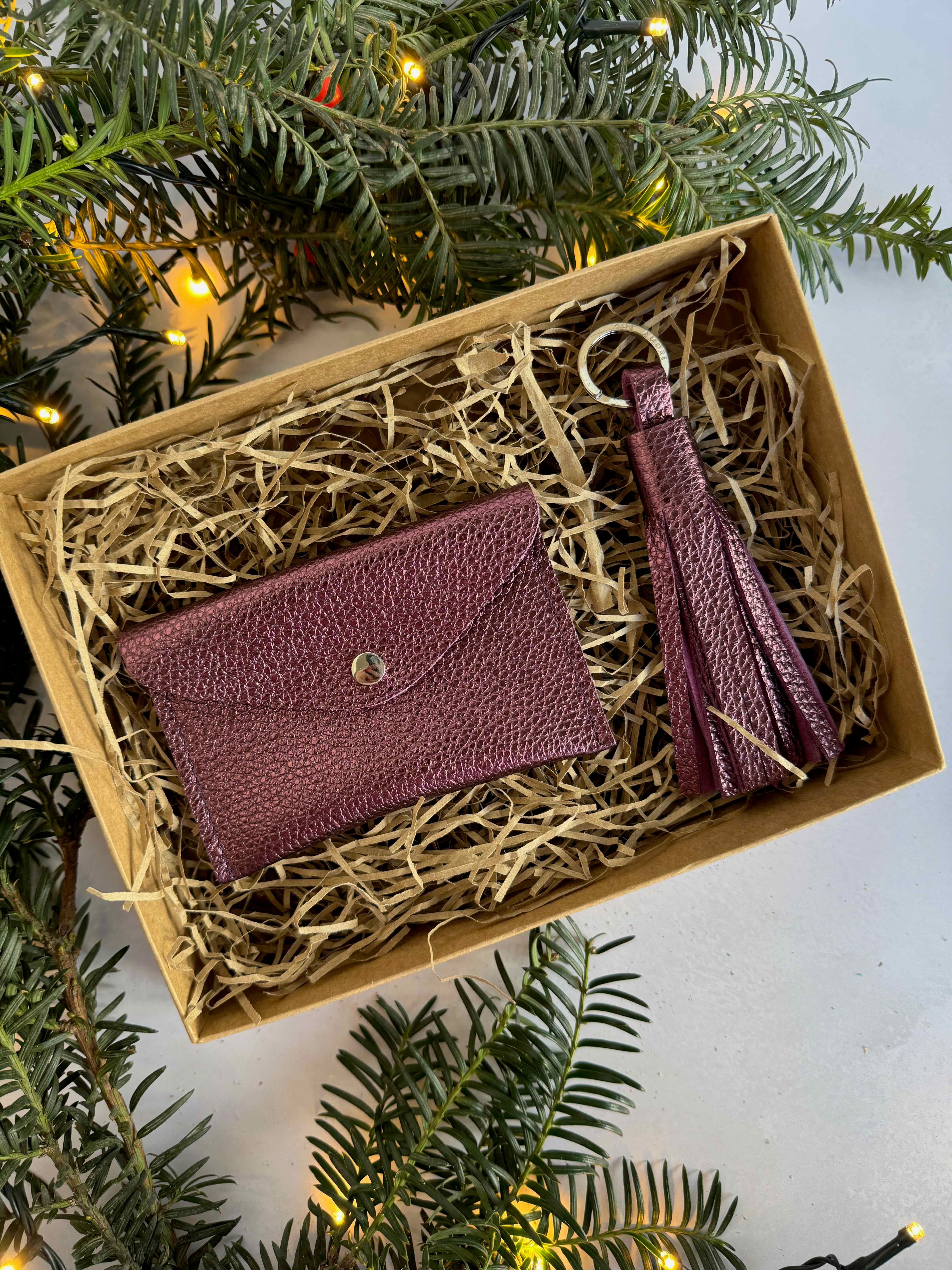 Metallic Purple wallet and keychain set in a box with Christmas tree branches and lights.