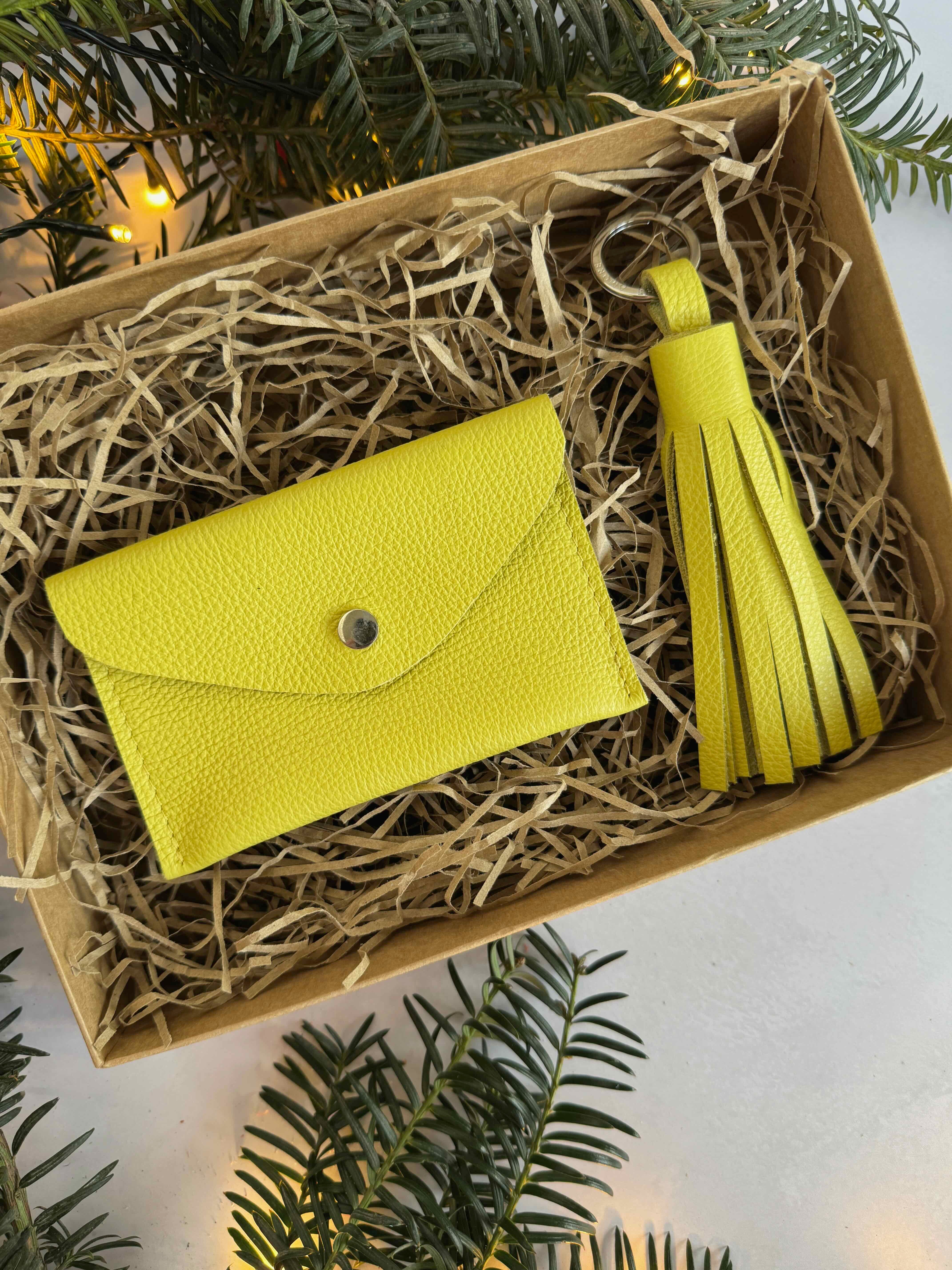 Yellow wallet and tassel in a box, surrounded by greenery.