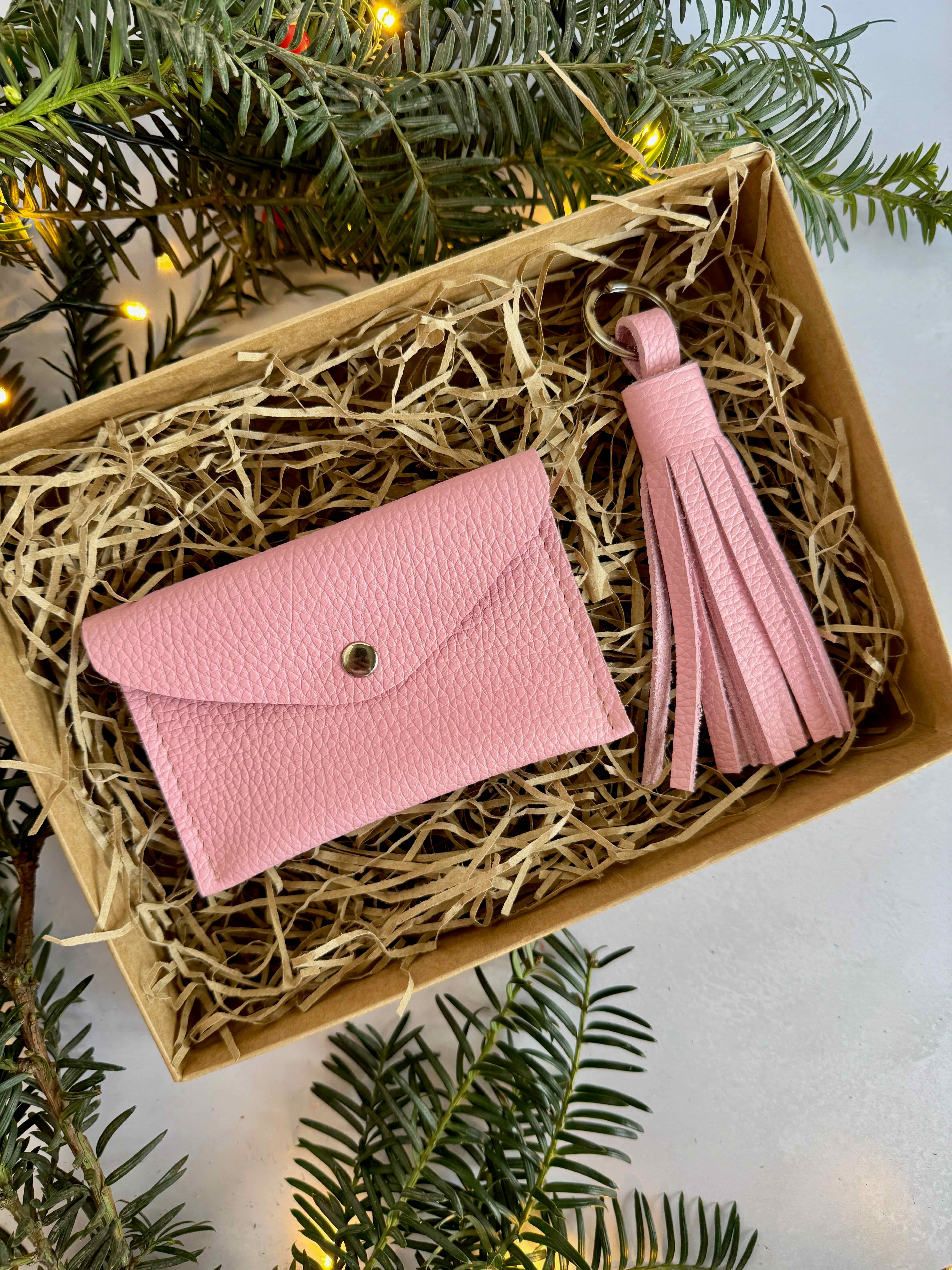 Pink wallet and tassel in a box surrounded by Christmas greenery