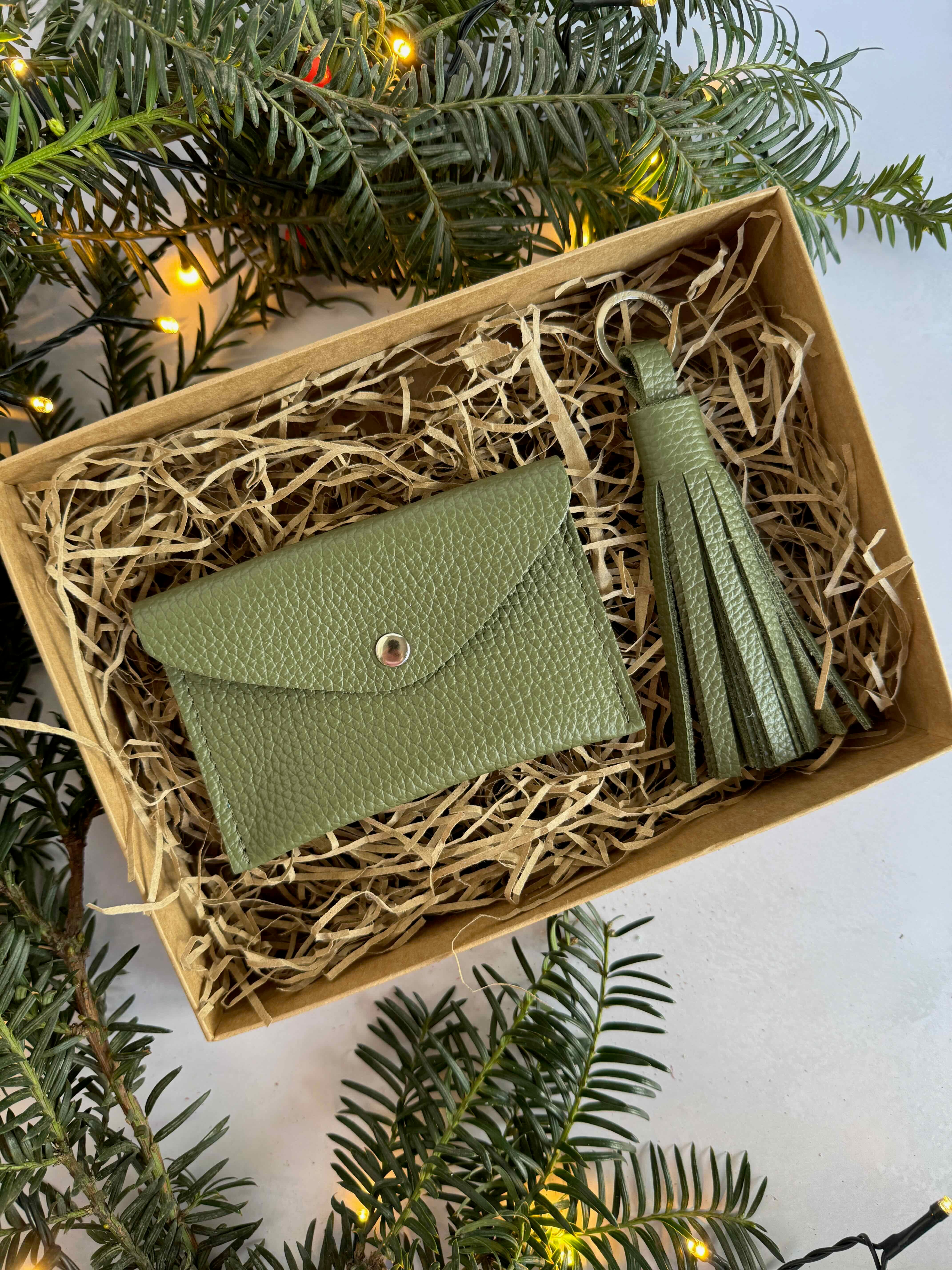 Green leather wallet and keychain set in a box with straw, surrounded by Christmas tree branches.