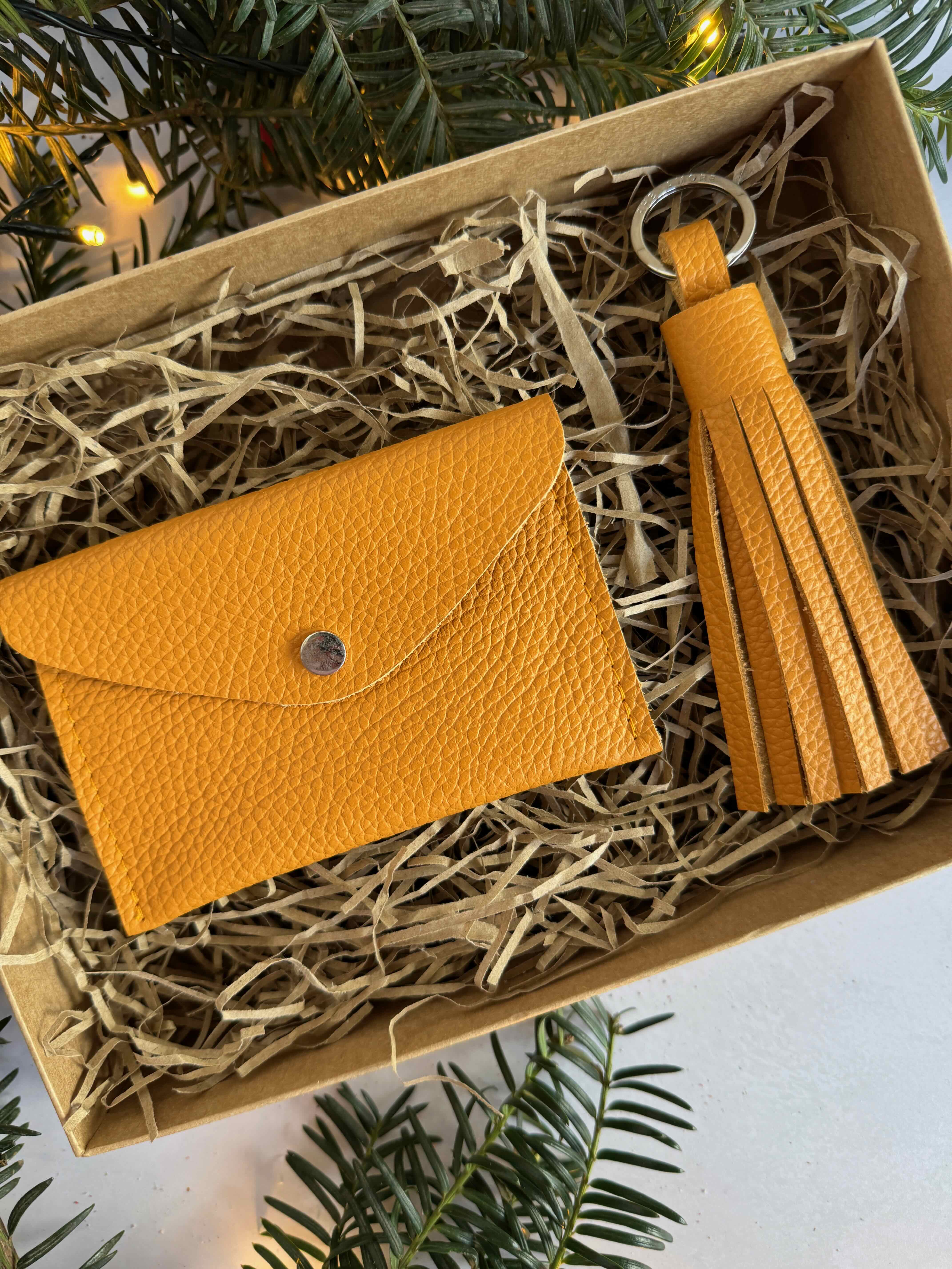 pumpkin spice orange leather wallet and tassel set in a box, surrounded by greenery.