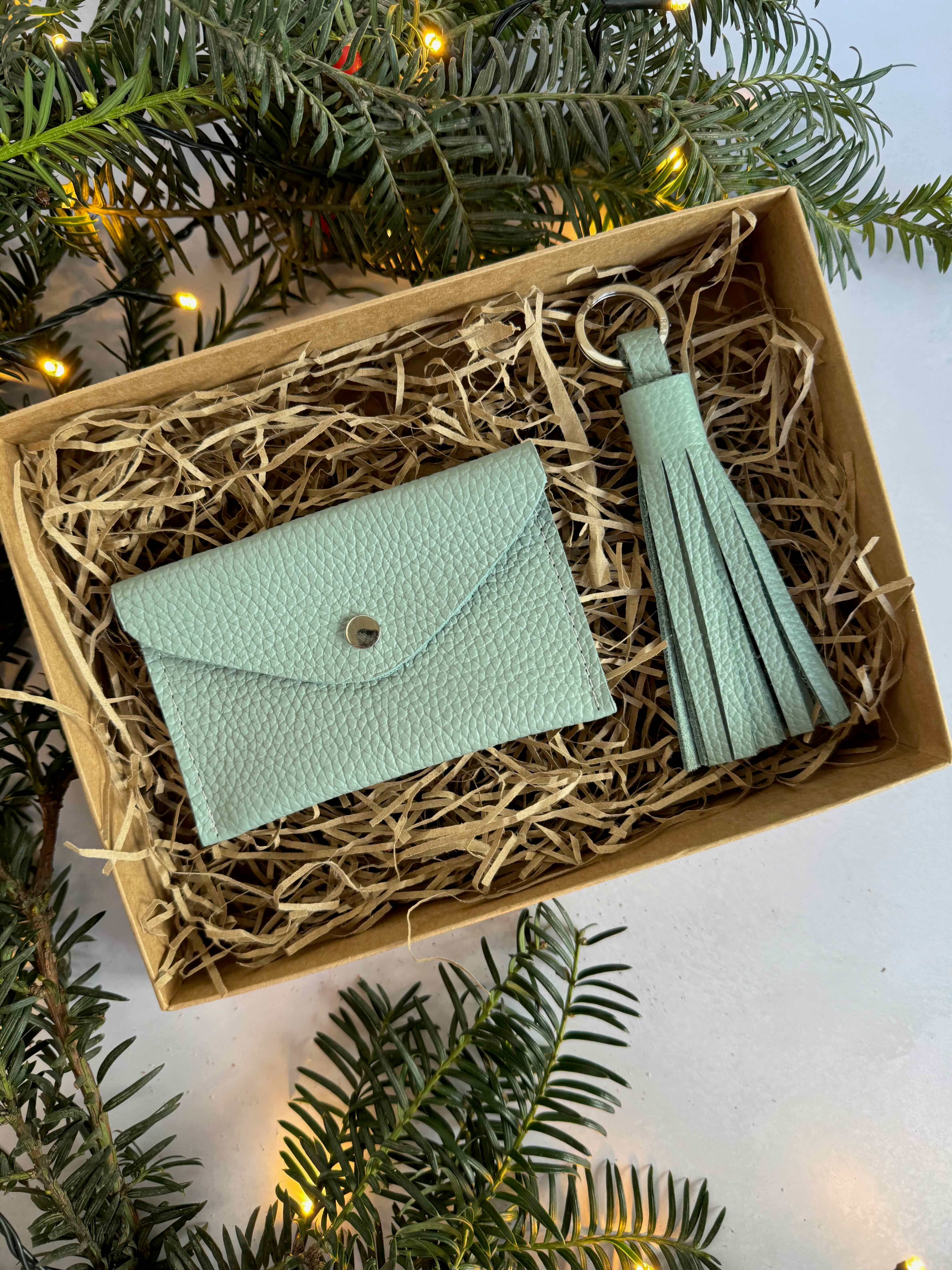 sage green wallet and tassel keychain in a box with Christmas tree branches.