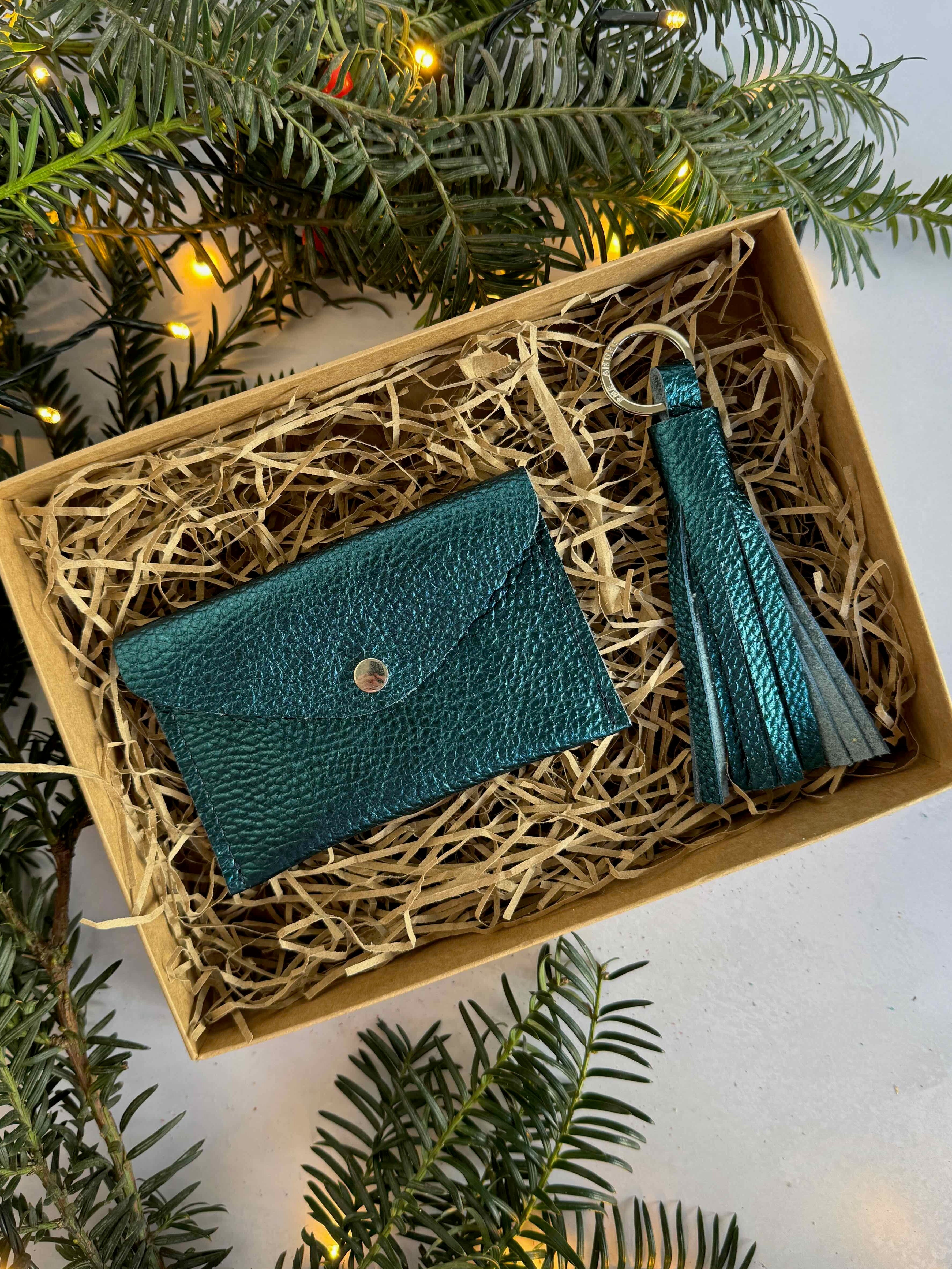 sapphire cardholder and tassel in a decorative box with Christmas tree branches and lights.