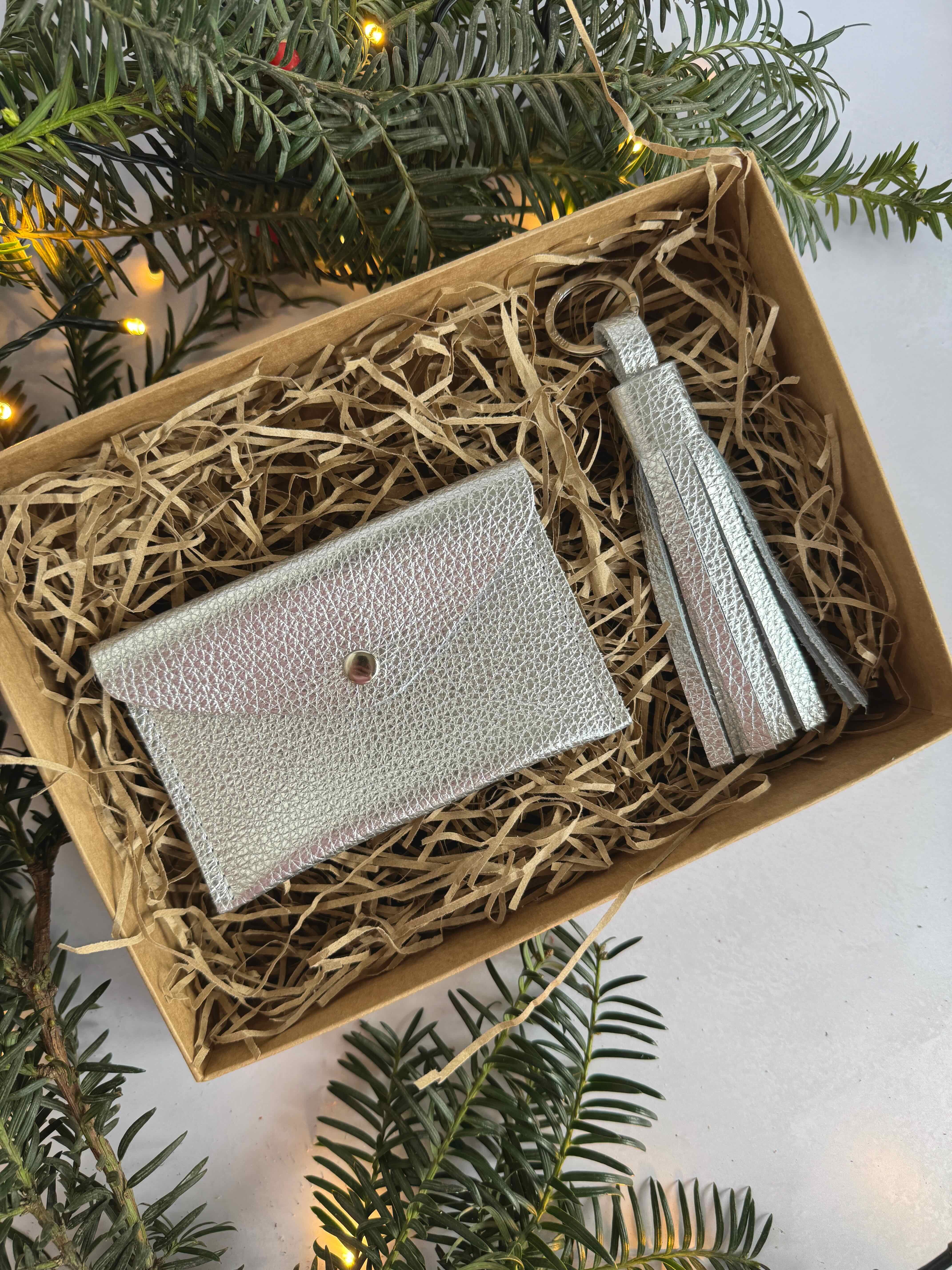 Silver wallet and tassel  set in a box with hay, surrounded by Christmas tree branches.