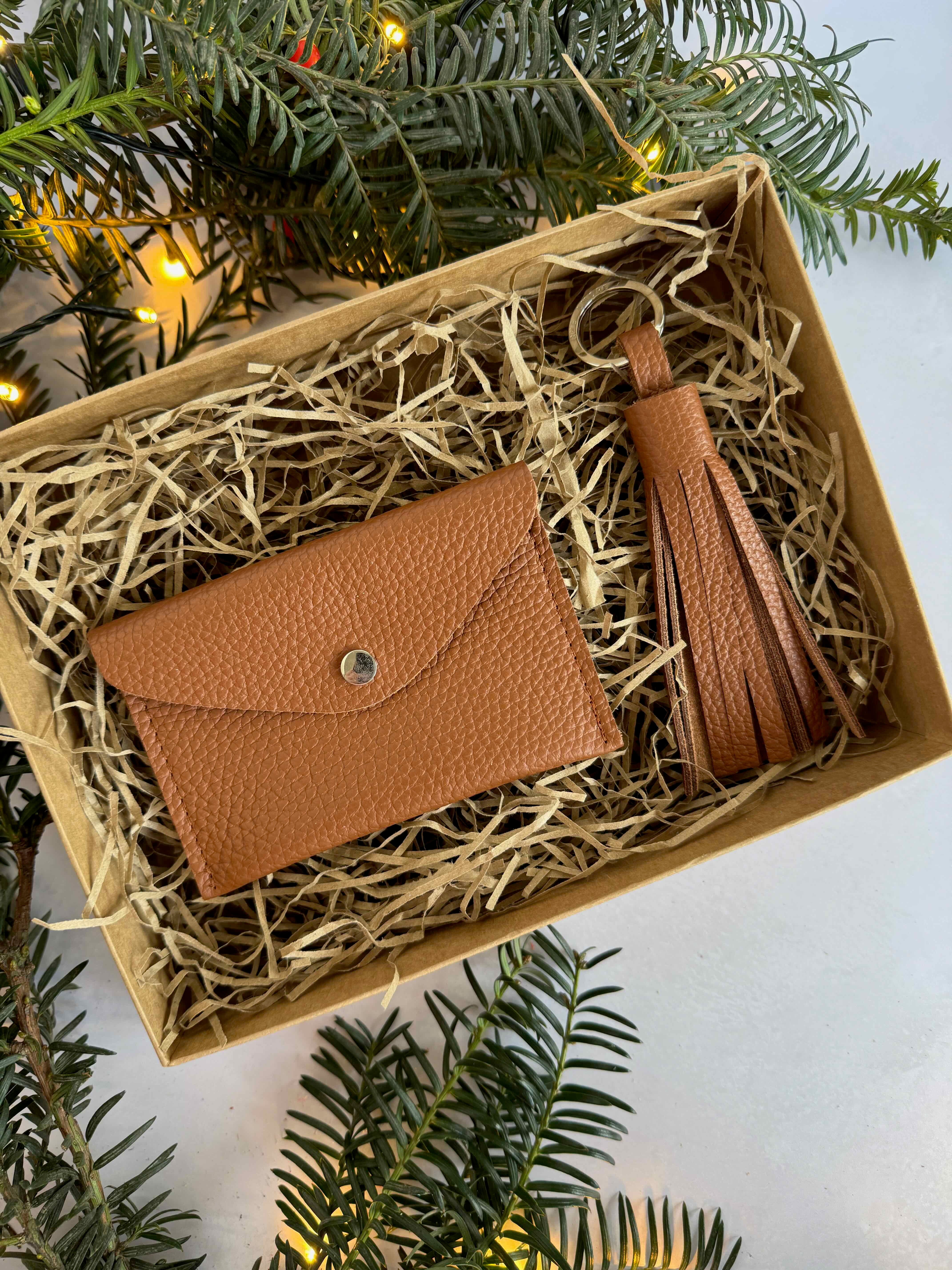 Brown leather wallet with tassel in a box surrounded by greenery