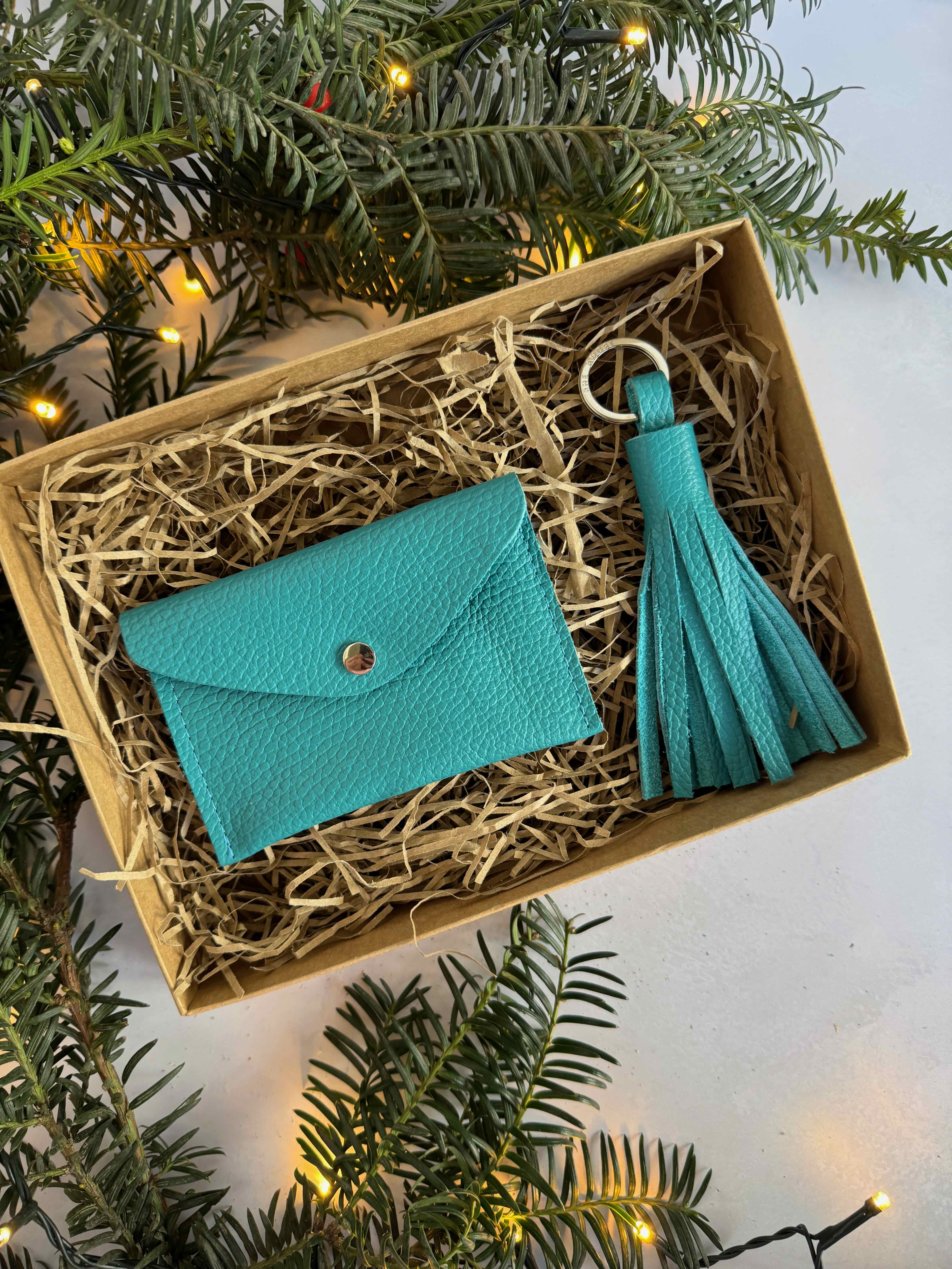 Turquoise wallet and keychain set in a decorative box with Christmas tree branches.